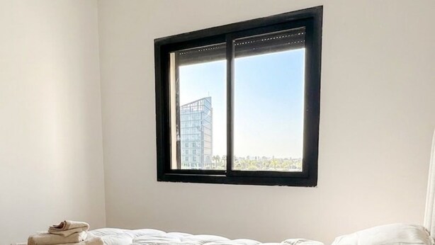 Un dormitorio con cama, ventana y vista a un edificio.