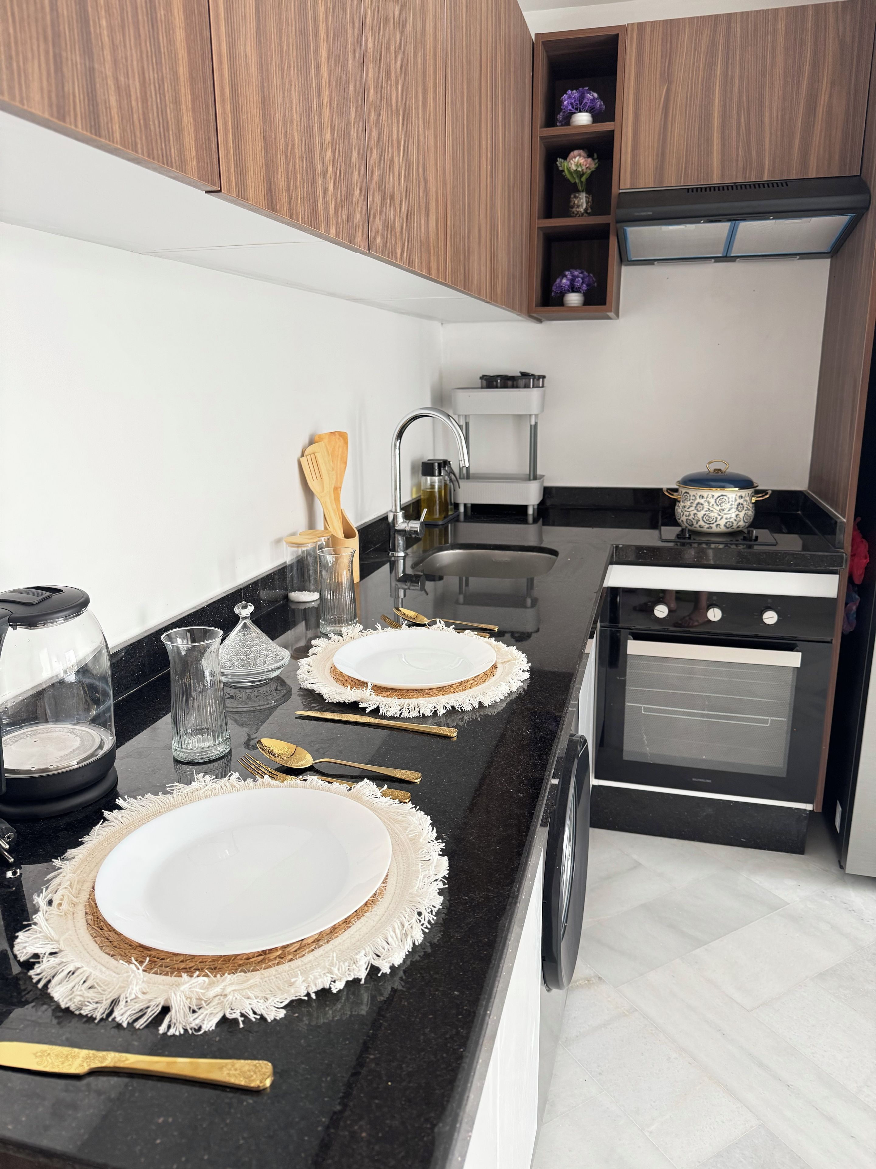Cozinha moderna com bancada preta, armários brancos, forno embutido e pia.