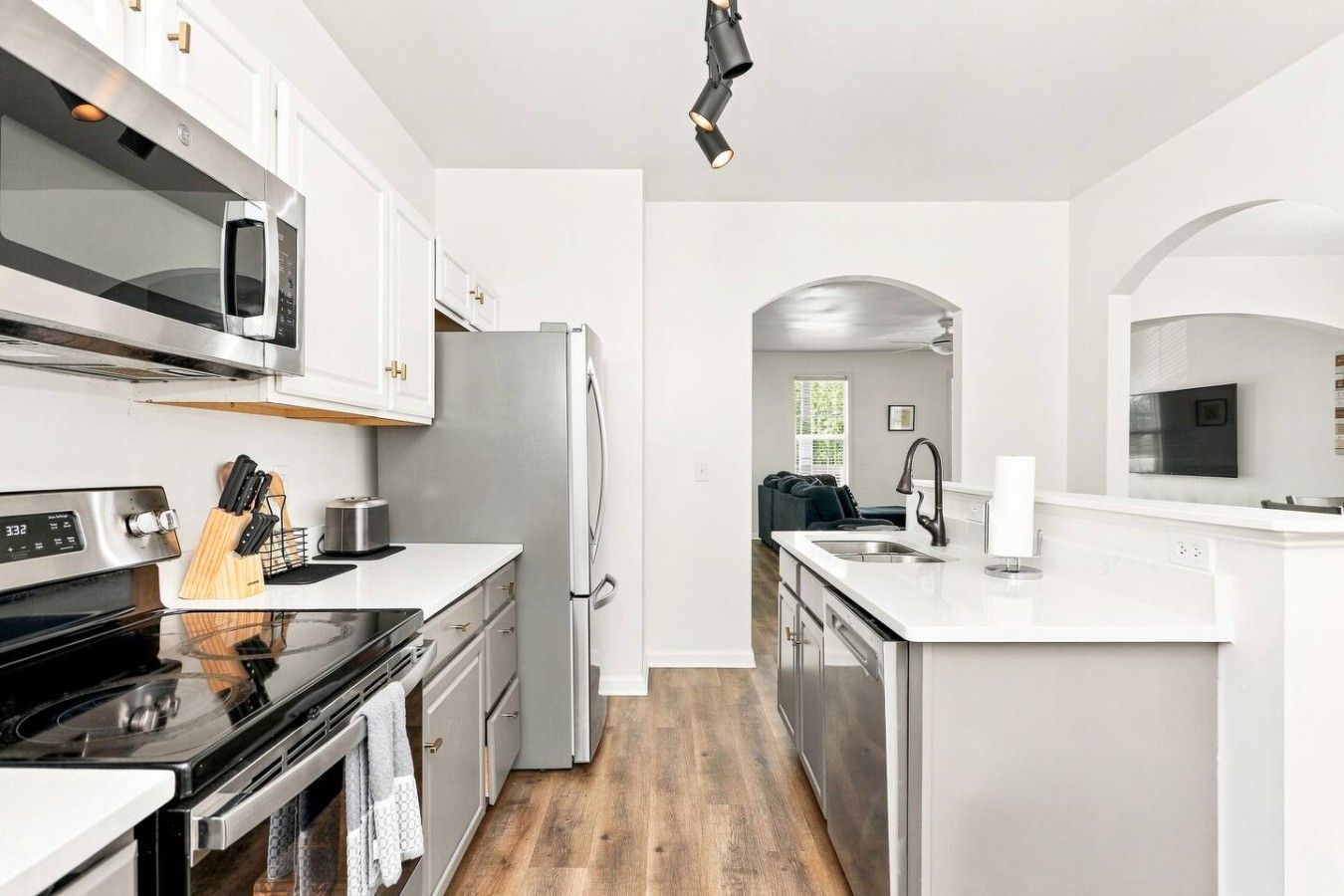 A modern kitchen with white cabinetry, stainless steel appliances, a black stove, and a wooden cutting board.