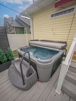 Un bain à remous sur une terrasse en bois, avec une maison en arrière-plan.