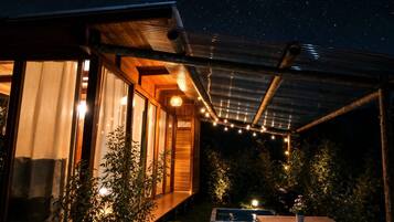 A wooden cabin with large windows, a covered patio, and a small pool.