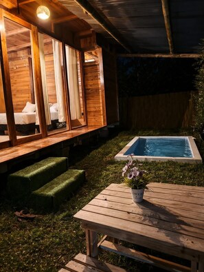 Una cabaña de madera con piscina, una mesa con maceta y un banco.