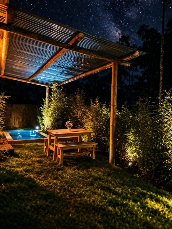 Un espacio al aire libre con piscina, mobiliario de madera y un cielo nocturno estrellado.