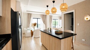 A modern kitchen with a central island, a dining area with a glass table, and pendant lighting. - Luxury Rooftop with Views of Cana: Pool, Sunset, Golf (Punta Cana)