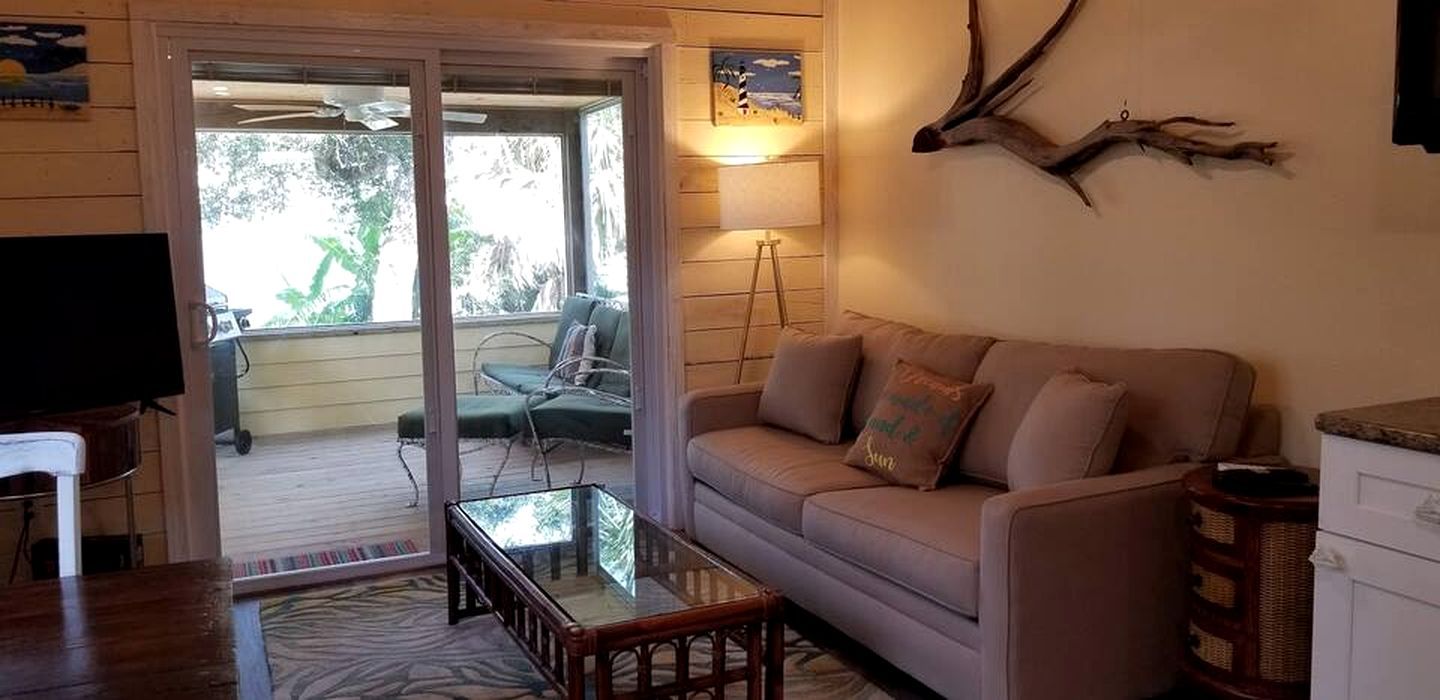 Un salon comprenant un canapé, une table basse en verre, un téléviseur et une vue sur une terrasse extérieure, accessible par une porte-fenêtre coulissante.