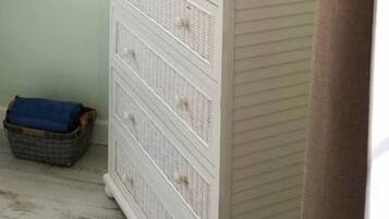 A room with a white dresser, a television on top, and an air conditioning unit on the wall.