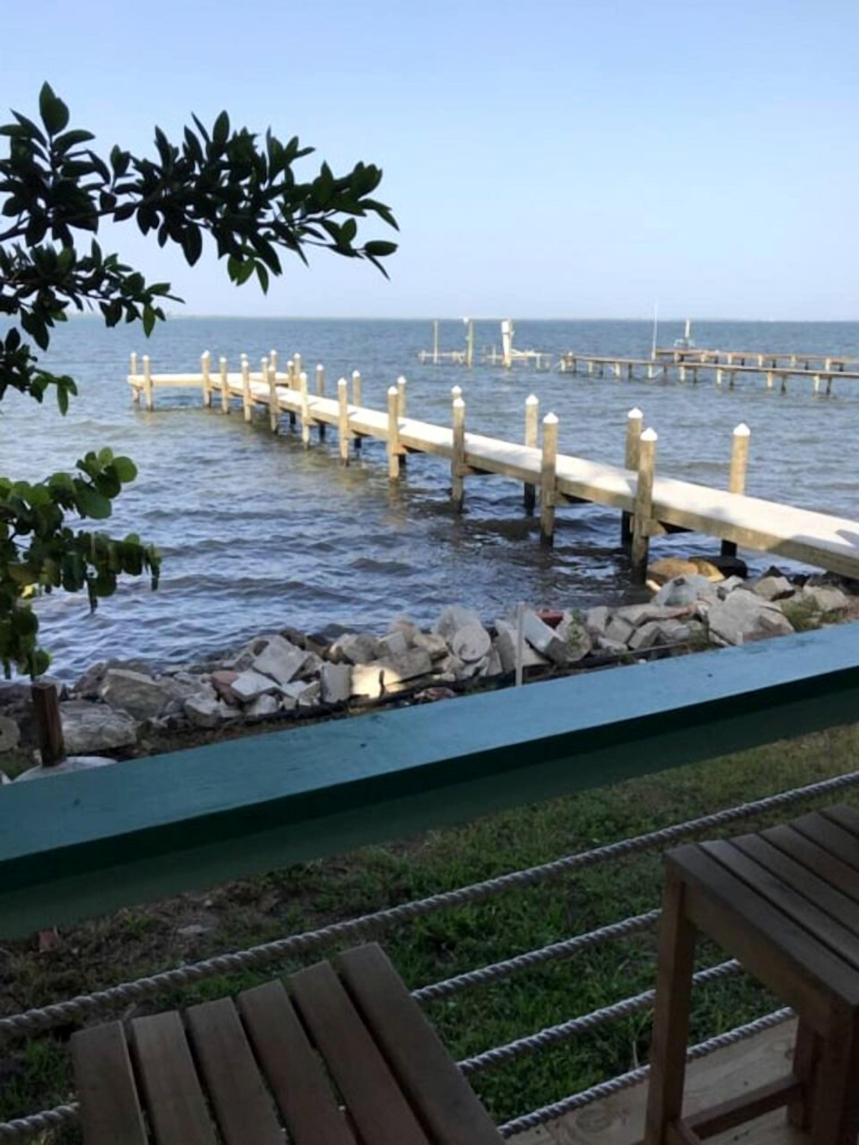 A wooden pier extending into calm water, surrounded by a stone wall and greenery.