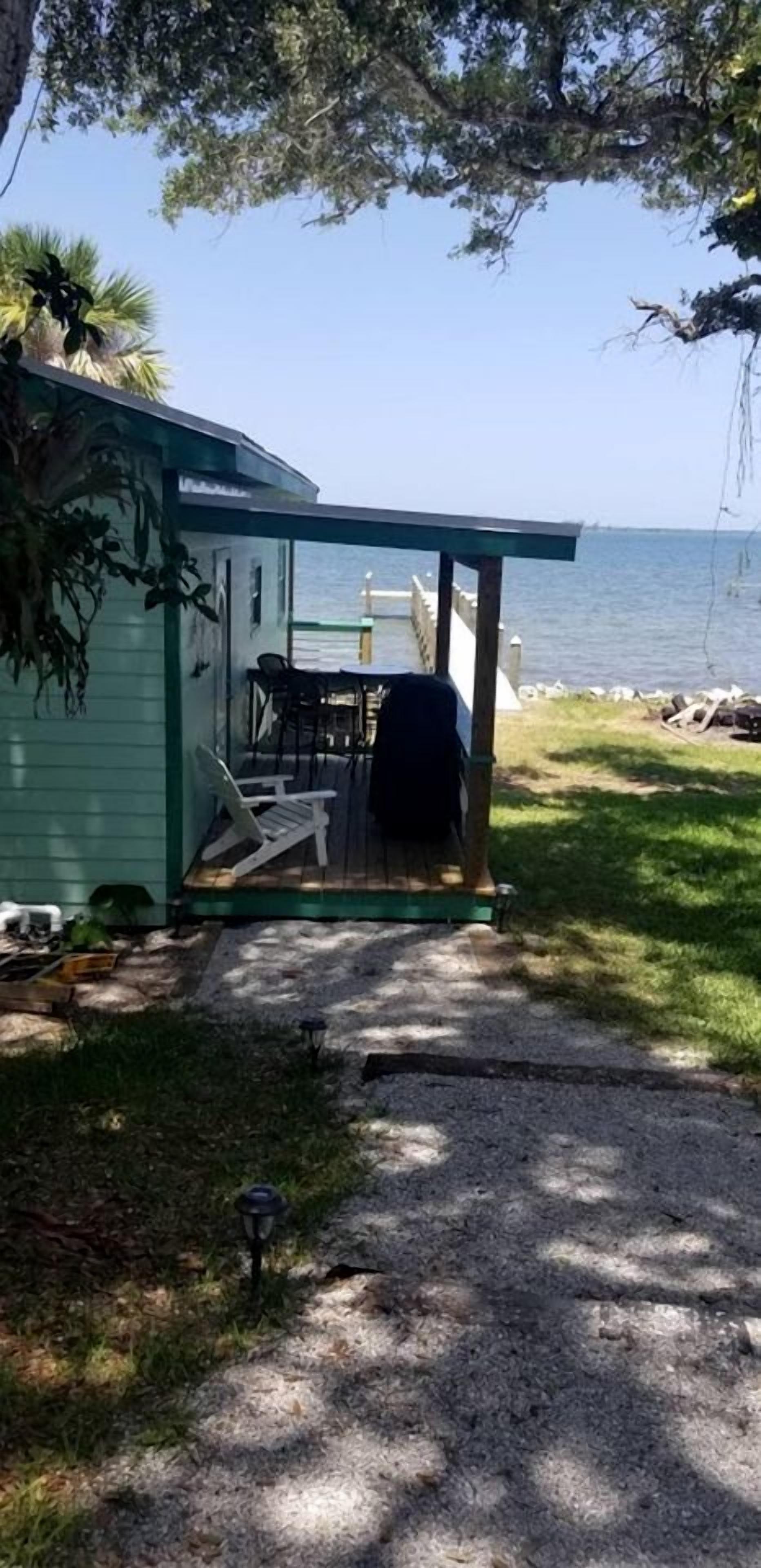Een overdekt buitengebied met een tafel, stoelen, een barbecue en uitzicht op het water.