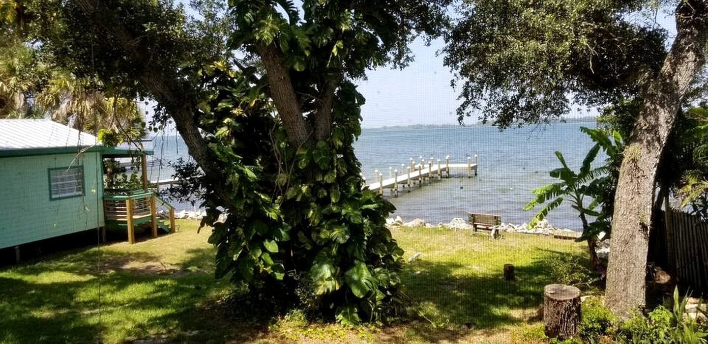 Une propriété située au bord d’un lac, avec un quai, un petit bâtiment et un grand arbre.