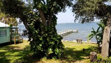 Une propriété située au bord d’un lac, avec un quai, un petit bâtiment et un grand arbre.