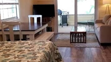 Een slaapkamer met een bed, een bureau, een televisie en een schuifdeur naar een patio.