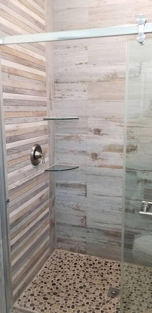 A shower with a glass door, a wooden wall, and a pebble-patterned floor. - Beautiful Waterfront Cottage for a Peaceful Romantic Escape in Micco, Florida (Micco)