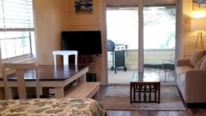 Et soveværelse med seng, skrivebord, fjernsyn og en skydedør, der fører ud til en patio.