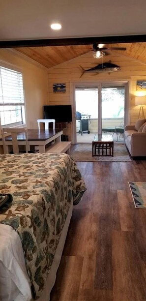 A bedroom with a bed, a desk, a television, and a sliding glass door leading to a patio area. - Beautiful Waterfront Cottage for a Peaceful Romantic Escape in Micco, Florida (Micco)