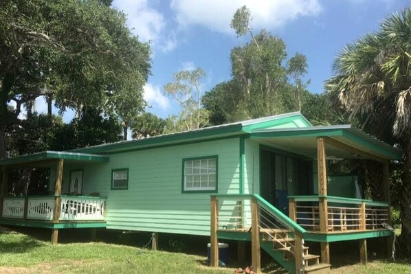 A green house with a porch, a staircase, and a fenced deck area. - Beautiful Waterfront Cottage for a Peaceful Romantic Escape in Micco, Florida (Micco)