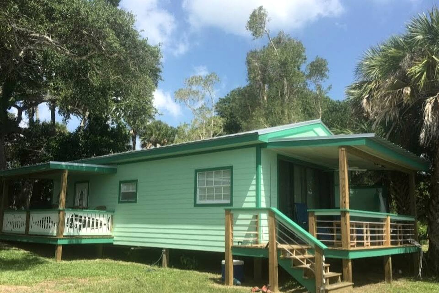 Een groene woning met een veranda, een trap en een omheind terras.