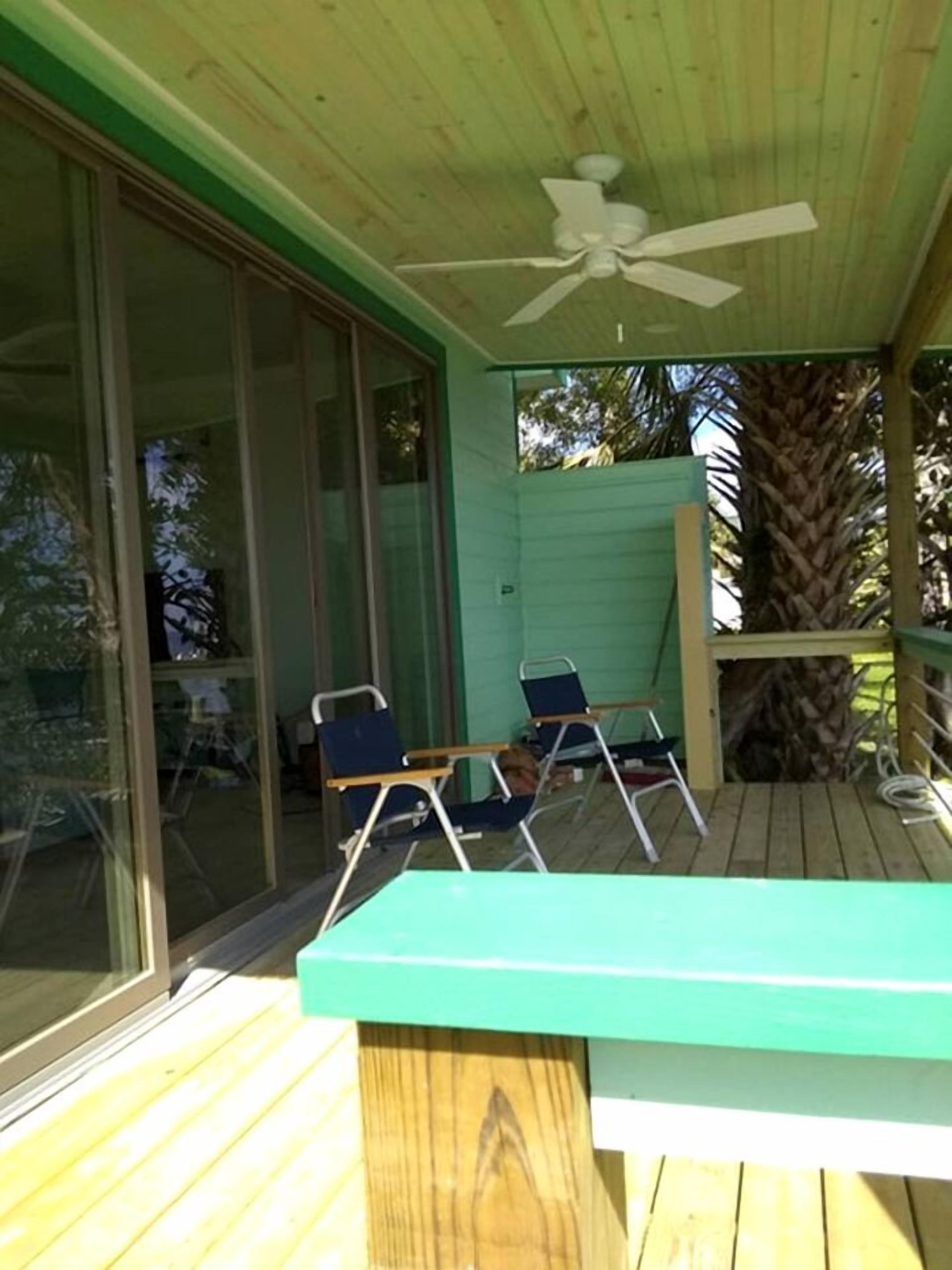 A covered outdoor area with a ceiling fan, a wooden deck, and two chairs.