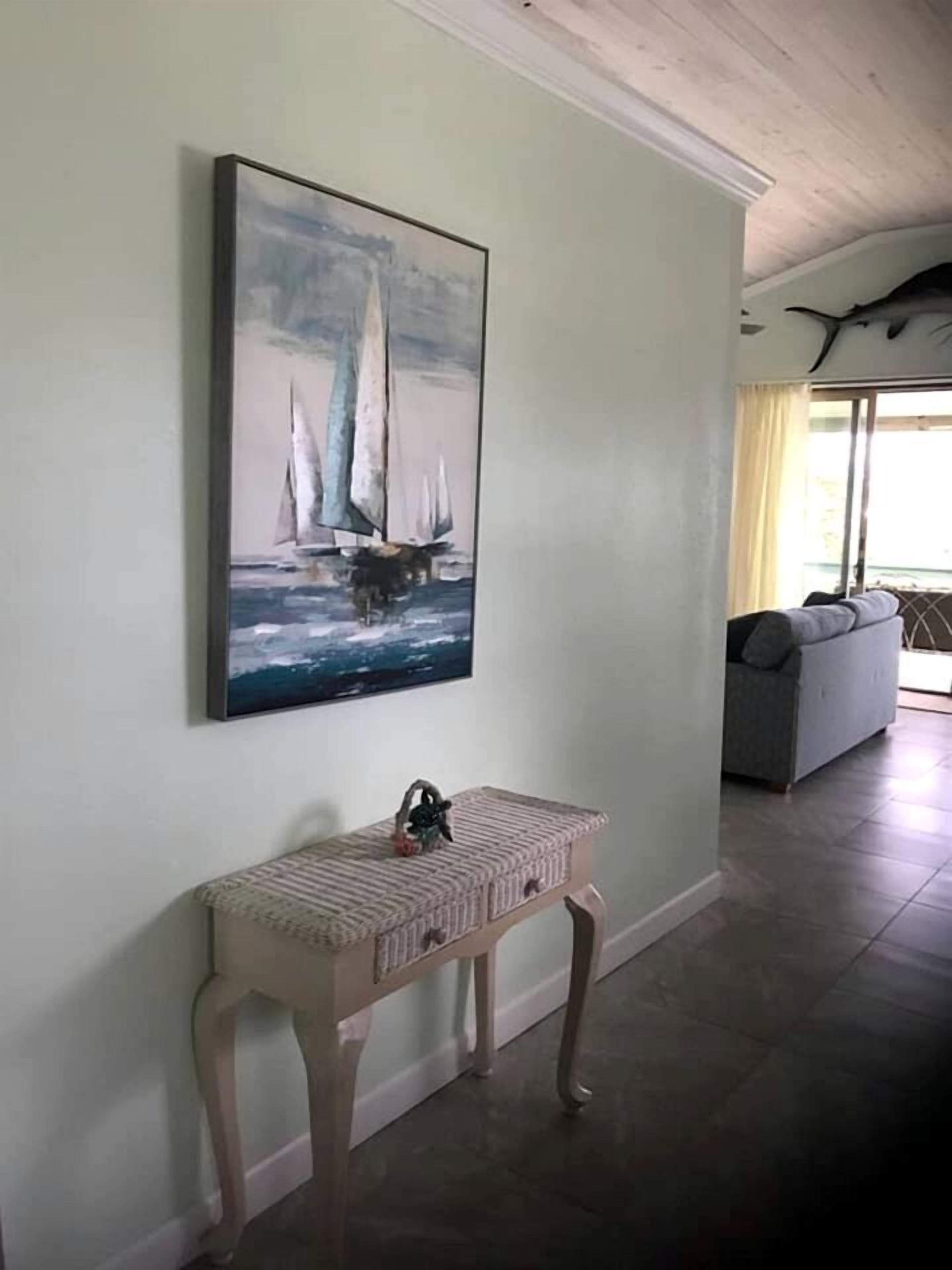 A hallway with a painting of sailboats on the wall, a small bench, and a sofa in the background.