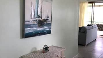 A hallway with a painting of sailboats on the wall, a small bench, and a sofa in the background.
