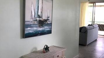 Un pasillo con un cuadro de veleros en la pared, un pequeño banco y un sofá al fondo.