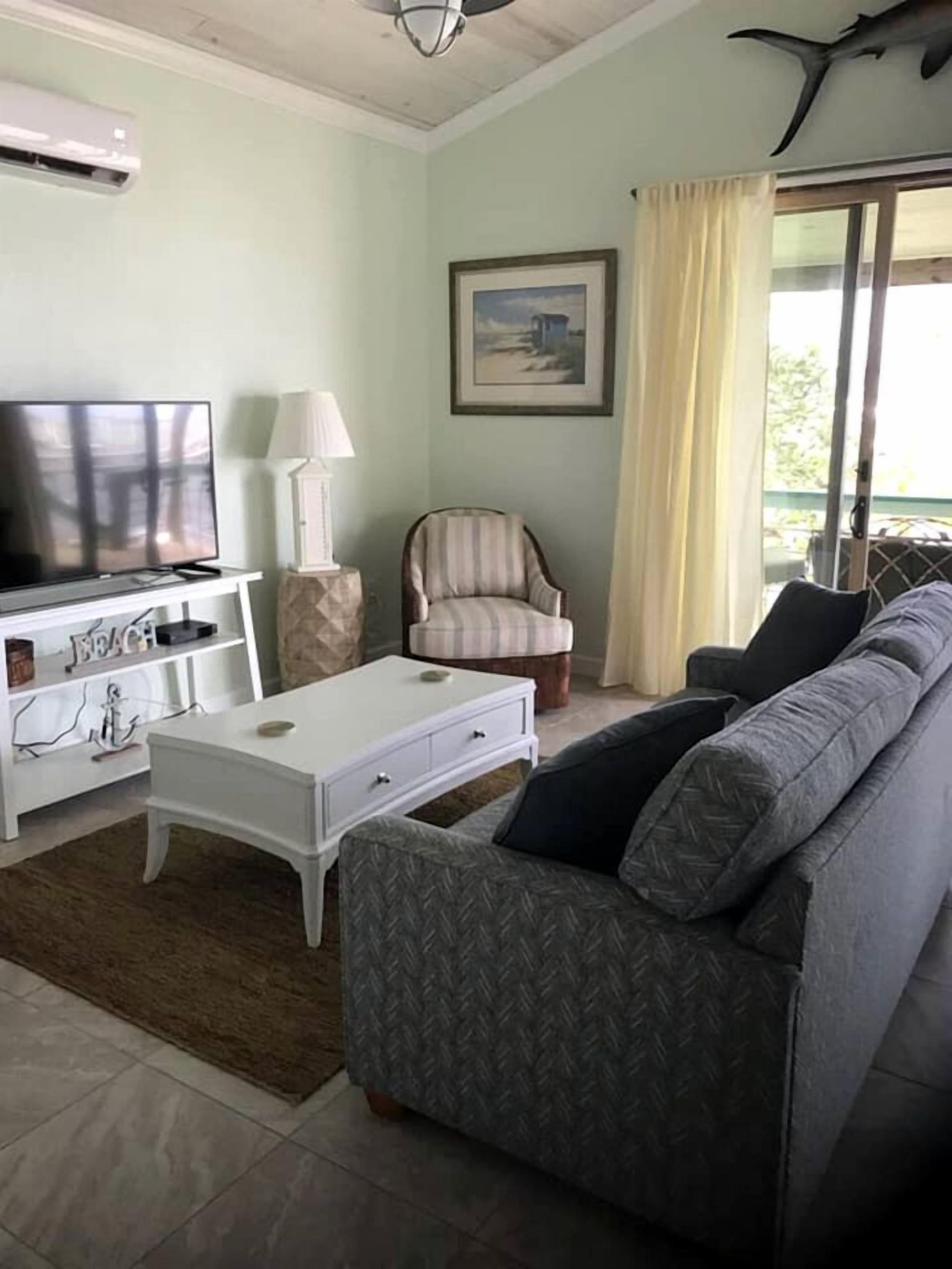 A living room with a television, a sofa, a chair, and a window with curtains.