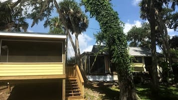 Casa móvel com escada de madeira para um deck, cercada por árvores e céu claro.