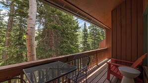 A wooden deck with a table and chairs, overlooking a forested area. - Superb 4-bedroom condo with AC in quaint Brian Head steps from Giant Steps Lodge (Brian Head)