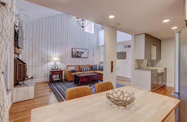 A modern living space with a wooden dining table, a sofa, and a kitchen area with a refrigerator.
