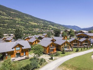 Eine Gruppe Holzhütten mit geneigten Dächern, umgeben von üppigem Grün und Bergen im Hintergrund.