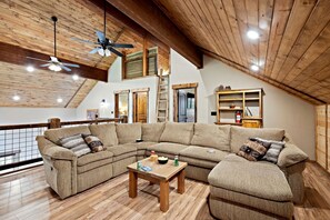 Ein geräumiges Wohnzimmer mit einem großen Ecksofa, Holzböden, einem Deckenventilator und einer Holzbibliothek.