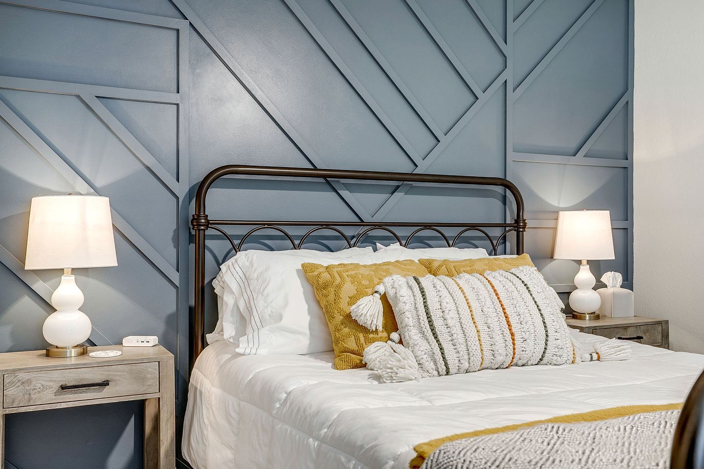 Un letto rifatto con cura, con biancheria da letto bianca e cuscini decorativi, affiancato da comodini con lampade e un piccolo cassetto.