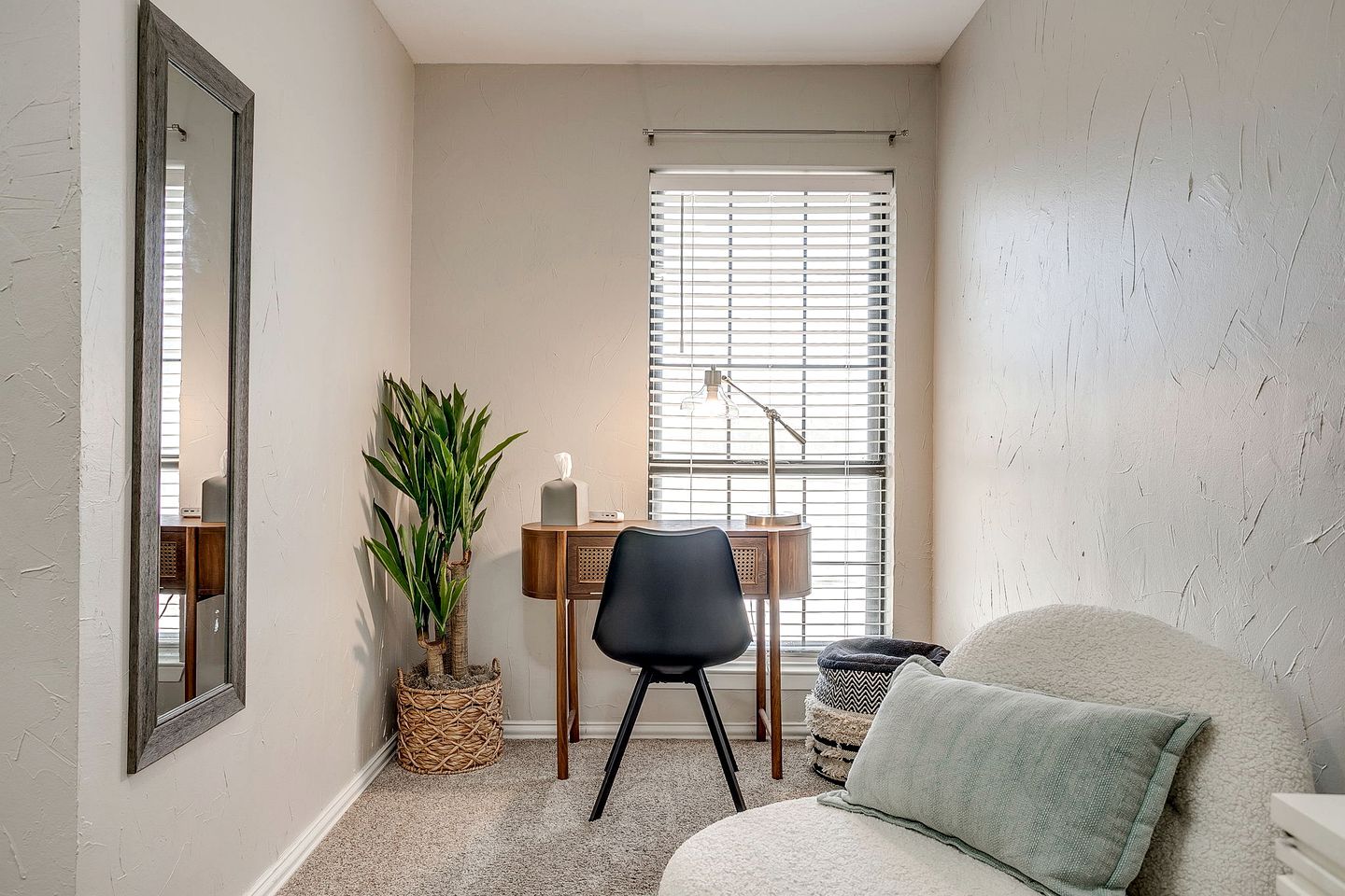 A corner room with a desk, chair, and a large window with blinds.