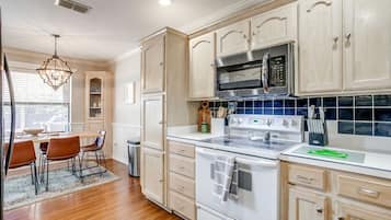 Une cuisine avec des meubles de rangement en bois, un four à micro-ondes, une cuisinière et un coin repas comprenant des chaises et une table.