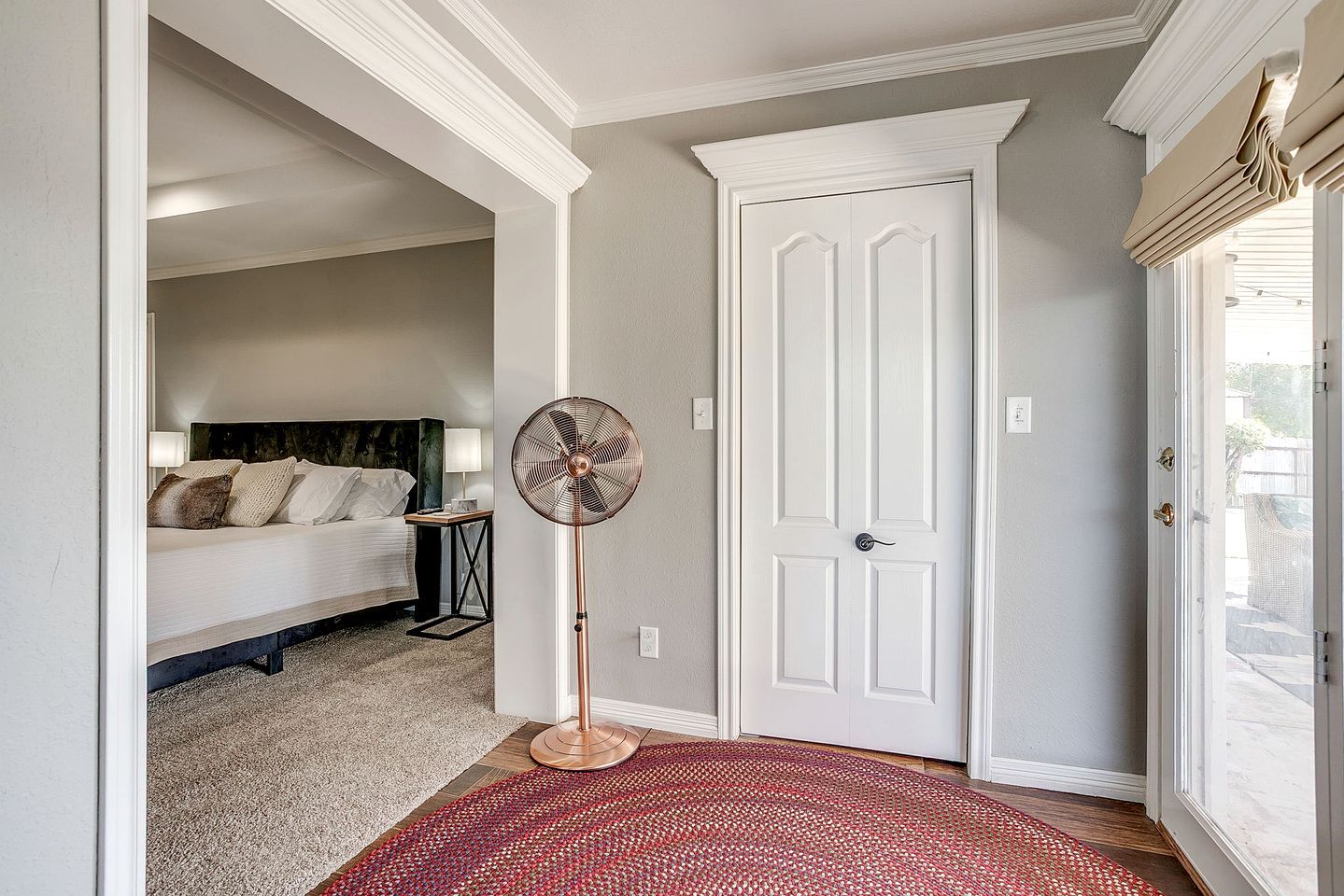 A hallway with a bed, a standing fan, and a door.