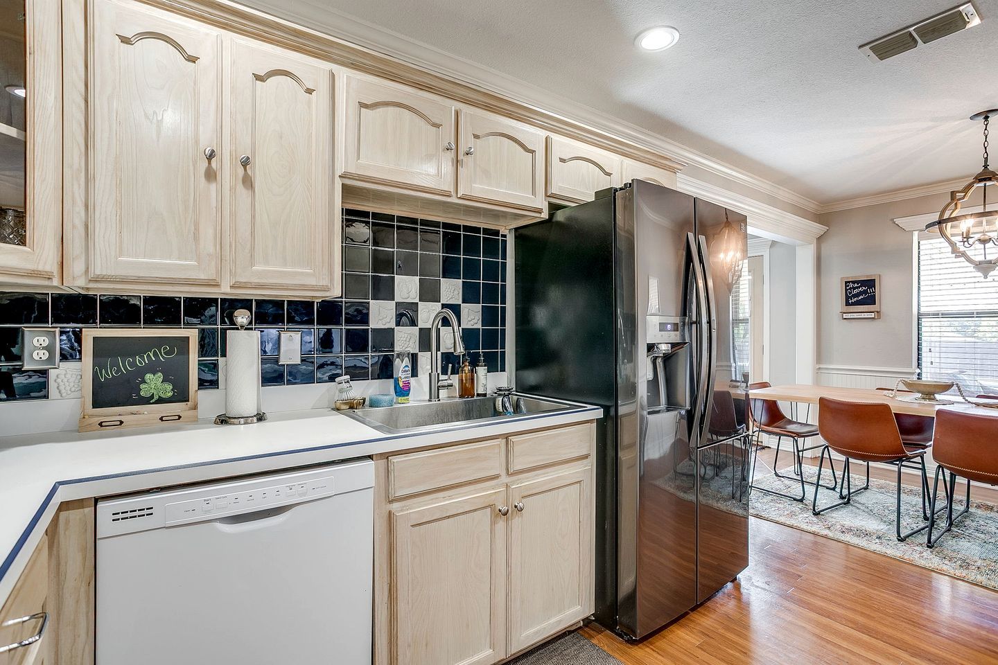 A kitchen with a stainless steel refrigerator, wooden cabinets, a tiled backsplash, and a chalkboard sign.