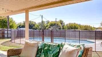 Un espace extérieur abrité comprenant une piscine, un canapé en osier avec des coussins et une clôture en bois.