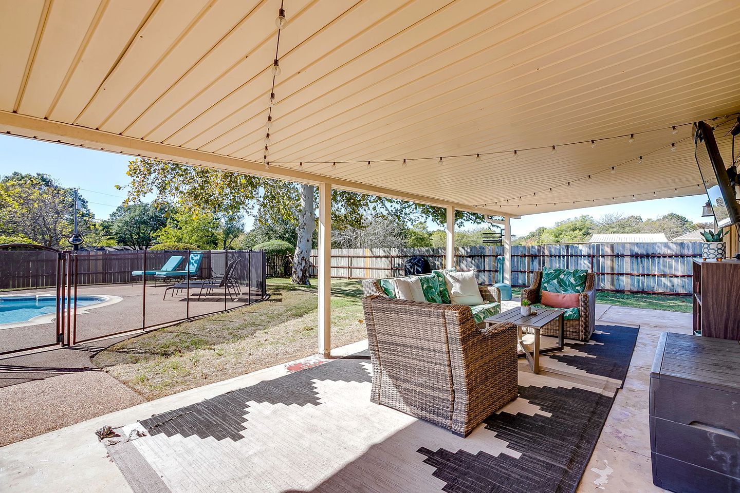 A covered outdoor patio with a pool, outdoor furniture, and a pergola with string lights.