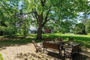 A paved outdoor area with wooden benches and a large tree providing shade. - Domaine 52 pers. | Rivière, Lac, Piscine (Saint-Félix-de-Kingsey)