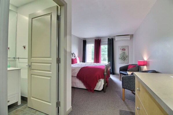A bedroom with a bed, a desk, a chair, and a bathroom with a toilet and sink. - Domaine 52 pers. | Rivière, Lac, Piscine (Saint-Félix-de-Kingsey)