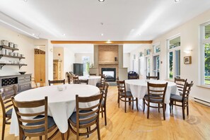 A dining area with round tables and chairs, a brick fireplace, and large windows.