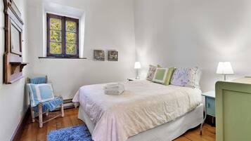 A bedroom with a bed, a chair, a window, and a nightstand.