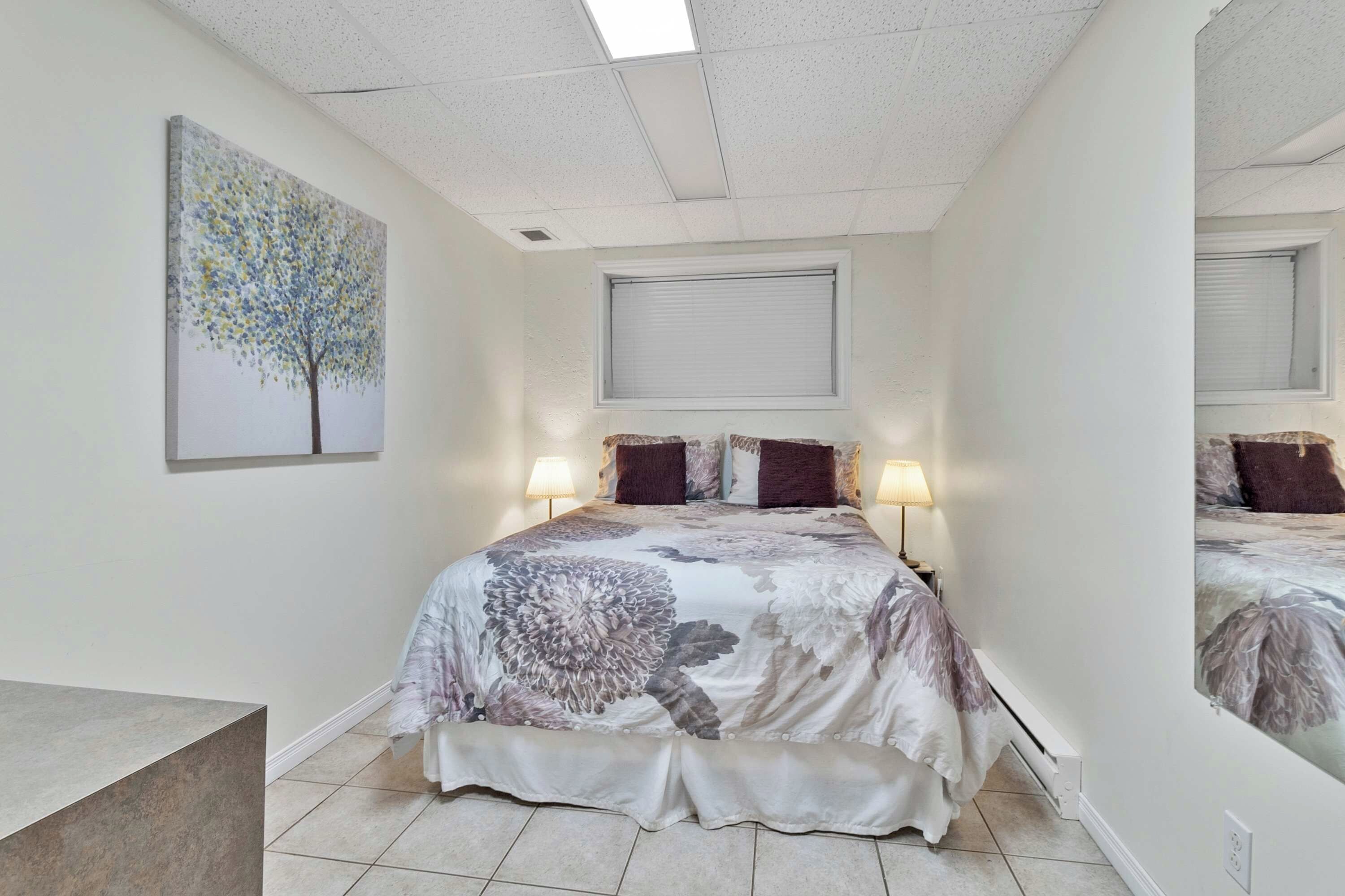 Une chambre à coucher avec un lit, deux lampes de chevet, une fenêtre avec des stores et un tableau au mur.