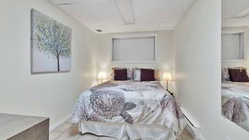 Une chambre à coucher avec un lit, deux lampes de chevet, une fenêtre avec des stores et un tableau au mur.