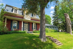 A two-story house with a front porch, a large tree, and a stone staircase leading to the entrance. - Domaine 52 pers. | Rivière, Lac, Piscine (Saint-Félix-de-Kingsey)