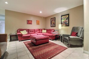 A living room with a red sectional sofa, a grey armchair, a patterned rug, and wall art. - Domaine 52 pers. | Rivière, Lac, Piscine (Saint-Félix-de-Kingsey)