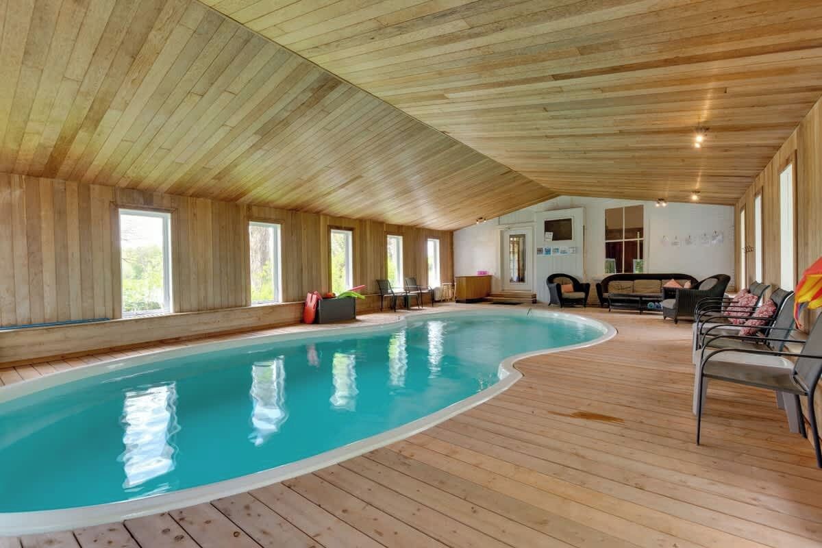 Une piscine intérieure aux murs et au plafond en bois, entourée d’espaces de détente et de grandes fenêtres.