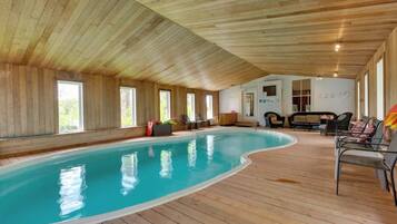 Une piscine intérieure aux murs et au plafond en bois, entourée d’espaces de détente et de grandes fenêtres.