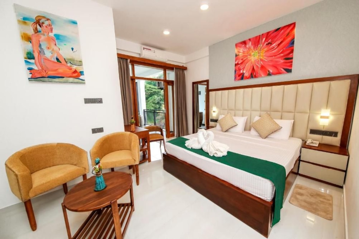 A hotel room with a large bed, two armchairs, a small table, and artwork on the walls.