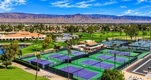 Un gran complejo deportivo con varias canchas de tenis, un campo de golf y una vista de montañas al fondo.