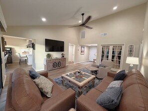 A living room with a brown sofa set, a coffee table, and a flat-screen TV mounted on the wall. - Rare 3BR Club Home: View, Golf, Tennis, Pools & Firepit (Palm Desert)